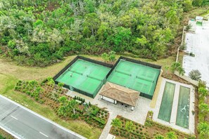 A tennis court complex with two courts, a covered seating area, and a swimming pool.