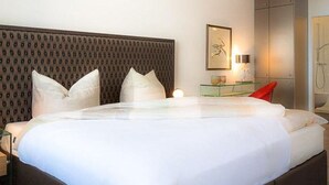 Ein modernes Hotelzimmer mit einem großen Bett, einer Kopfstütze mit Muster, einem Nachttisch mit Lampe und einem gerahmten Bild an der Wand.
