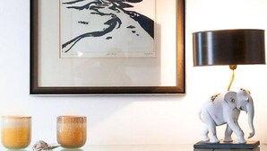 Ein gerahmtes Kunstwerk, eine Lampe und eine Skulptur auf einem Regal.