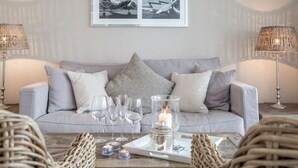 A living room with a grey sofa, two lamps, a tray with glasses and a candle, and a wall with a framed picture.
