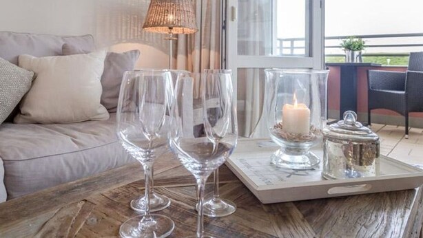 A wooden table with three wine glasses, a lit candle, and a tray with a candle and a container.