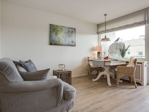 Un salón con un sofá gris, una mesa de comedor con una silla, una lámpara y un cuadro de un mapa del mundo en la pared.