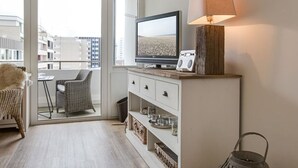 A modern hotel room with a balcony, a television, a lamp, and a wicker chair. - New Port II - Newport on the beach with south-facing balcony and dune view (Sylt)