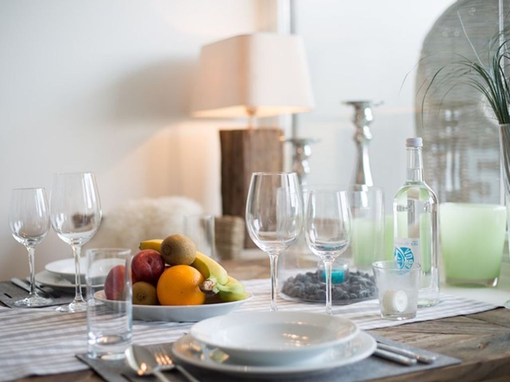 A dining table set with plates, cutlery, glasses, and a fruit bowl.