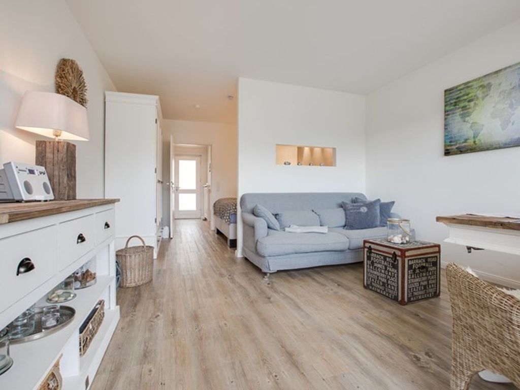 A modern living room with a light blue sofa, a white cabinet with drawers, a wooden coffee table, and a wicker chair.
