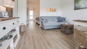 A modern living room with a light blue sofa, a white cabinet with drawers, a wooden coffee table, and a wicker chair. - New Port II - Newport on the beach with south-facing balcony and dune view (Sylt)