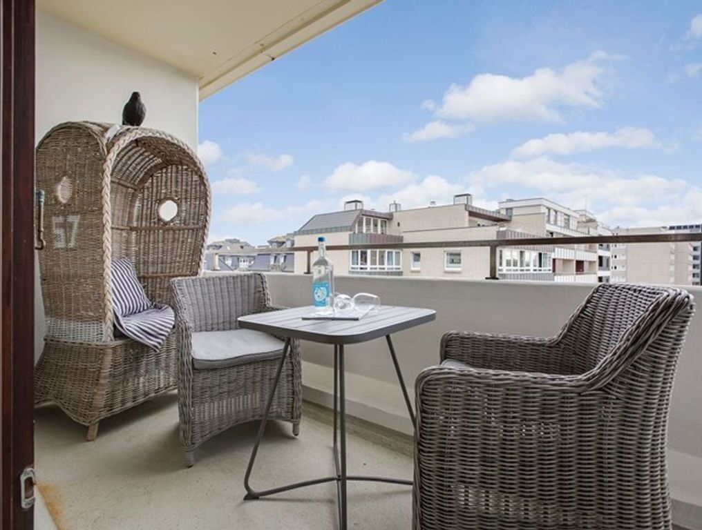A balcony with wicker furniture, a table, and a view of buildings.