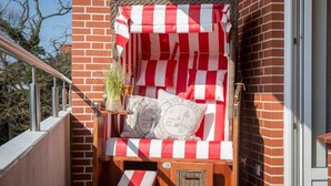 A red and white striped outdoor seating area with a wicker chair, a small table with a plant, and decorative pillows. - Nordstern - 1-room apartment with balcony and beach chair in the immediate vicinity (Sylt)