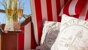 A bed with red and white striped bedding, two pillows with text, and a nightstand with glasses and a vase of flowers. - Nordstern - 1-room apartment with balcony and beach chair in the immediate vicinity (Sylt)