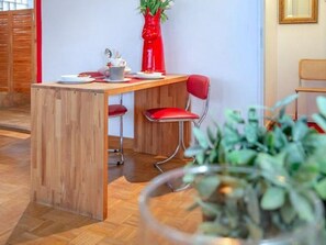 A wooden dining table with two red chairs, a red vase, and a potted plant in the foreground. - Strandgeflüster - STRANDGEFLÜSTER: Strandstraße, modern 2 room apartment (Sylt)