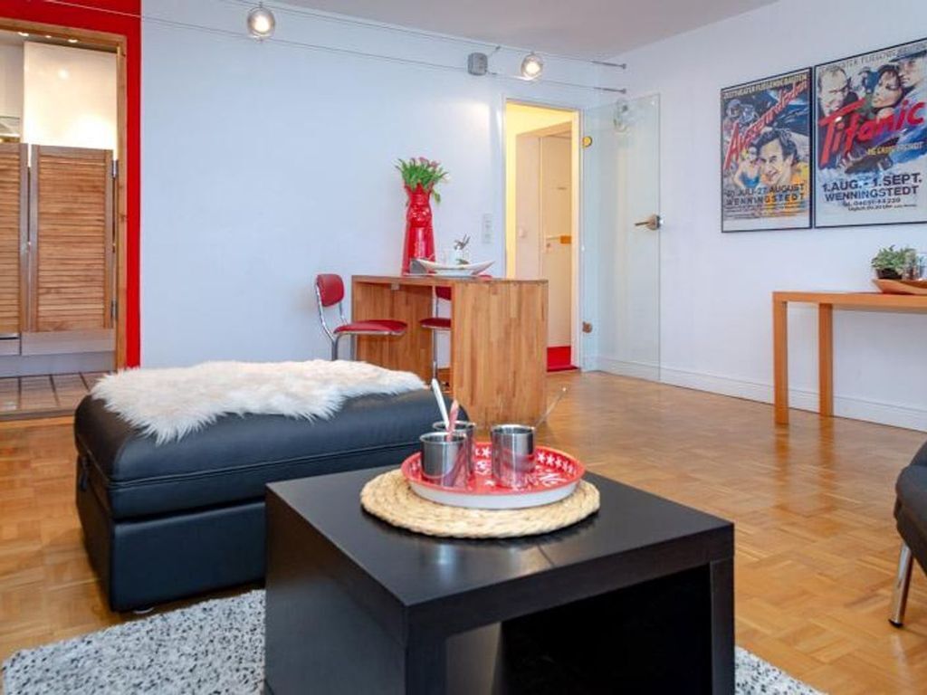 A modern living room with a black sofa, a small coffee table with a tray, a wooden dining table, and a red chair.