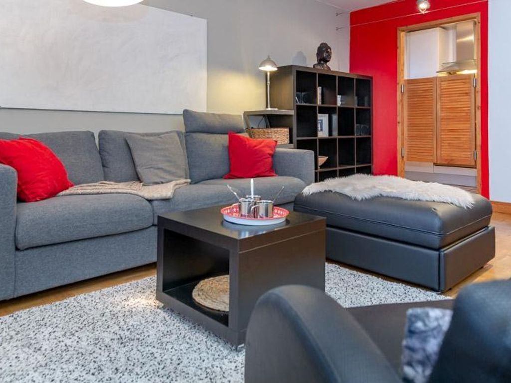 A modern living room with a grey sofa, red cushions, a black ottoman, and a coffee table with a tray.