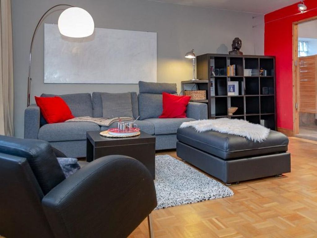 A modern living room with a grey sofa, red cushions, a black ottoman, a coffee table, and a bookshelf.