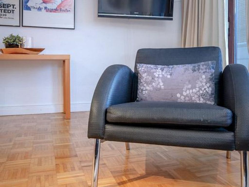 A modern living room with a dark grey armchair, a wooden side table with a plant, and a framed picture on the wall.
