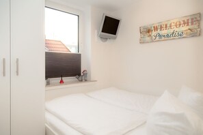 Une chambre avec un lit, un téléviseur fixé au mur, une fenêtre avec des stores et une pancarte indiquant « Bienvenue au paradis ».
