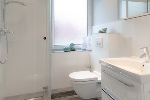 Un bagno moderno con cabina doccia in vetro, un water e un lavandino con specchio sopra.