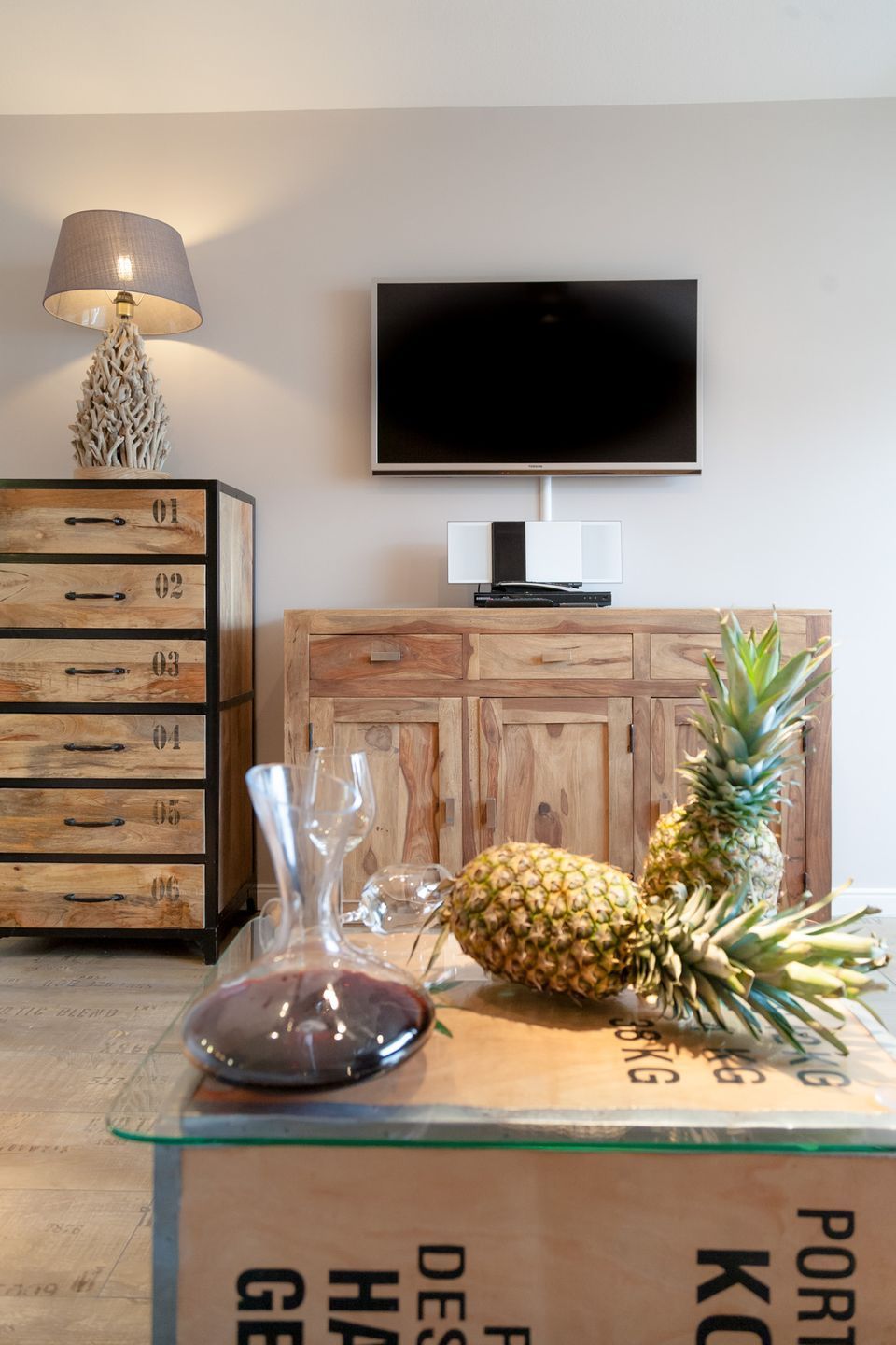A modern living room with a wooden cabinet, a television, and a pineapple on a glass table.