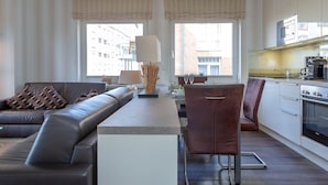 Un salon moderne comprenant un canapé, une table à manger avec des chaises, une lampe et un coin cuisine équipé d’appareils électroménagers.