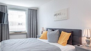 En pænt redt seng med stribet sengetøj, en grå sengegavl og to sengeborde med lamper.