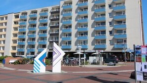 Et hotel med flere etager, altaner, en central indgang og en parkeringsplads.