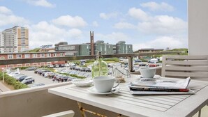 A balcony with a table set for two, overlooking a parking lot and buildings.