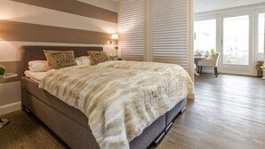 A bedroom with a large bed, a nightstand, a lamp, and a view of the outdoors through a sliding door.