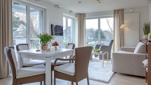 A modern living room with a white dining table, wicker chairs, a white sofa, and a balcony with a view. - Viktoria Residence, App. 10 - Top city location: Very comfortable, bright 2 (Sylt)
