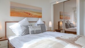 A neatly arranged bedroom with a large bed, two bedside tables, a nightstand, a mirror, and a painting on the wall. - Viktoria Residence, App. 10 - Top city location: Very comfortable, bright 2 (Sylt)