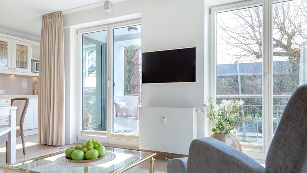 A modern living room with a glass coffee table, a grey sofa, and a flat-screen TV mounted on the wall. - Viktoria Residence, App. 10 - Top city location: Very comfortable, bright 2 (Sylt)