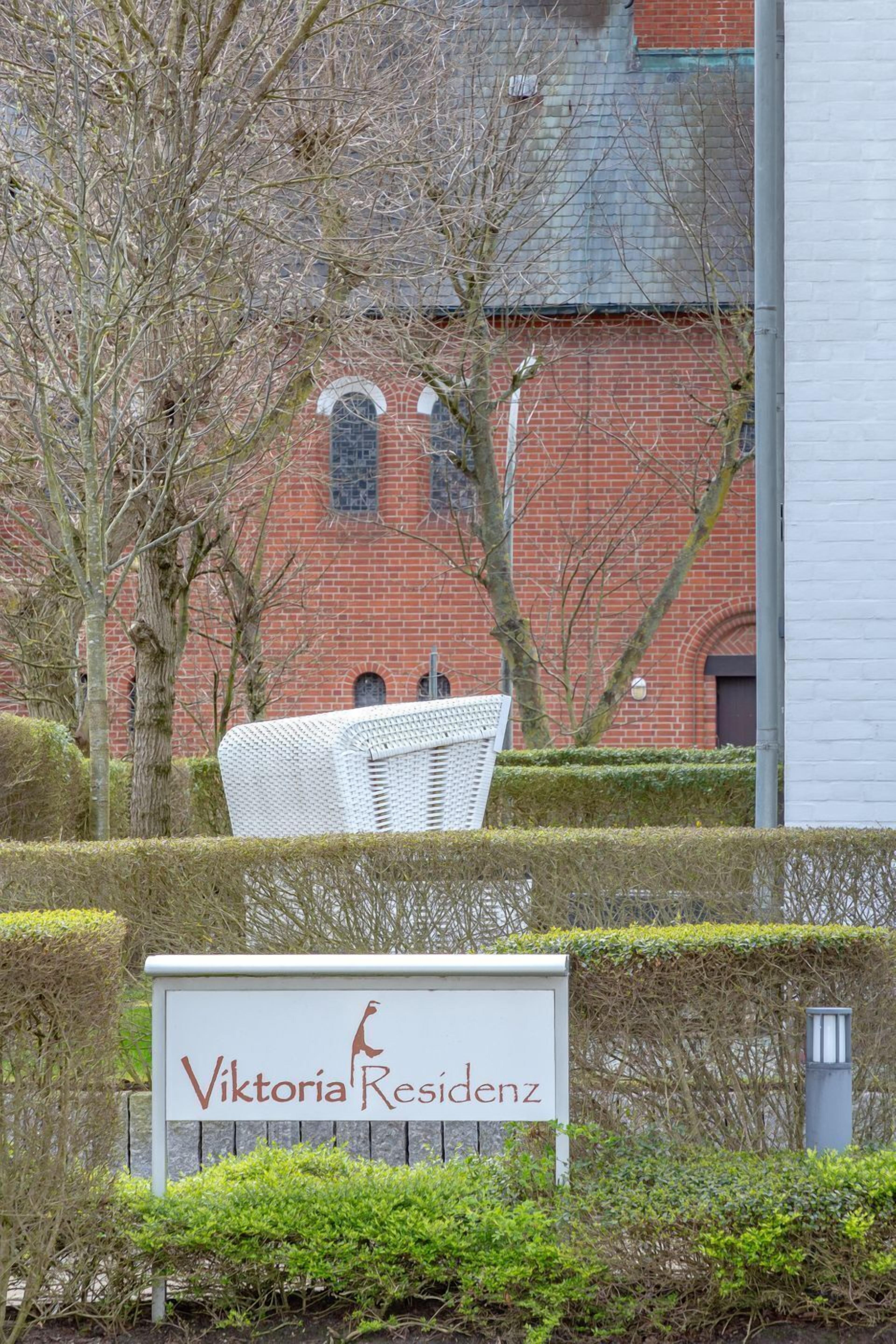 Une enseigne indiquant l’emplacement de l’hôtel Viktoria Residenz, avec une chaise en osier blanche placée au premier plan.
