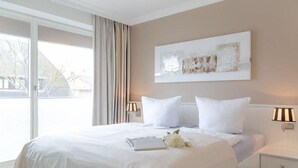 A neatly made bed with white linens and pillows, a bedside lamp, and a framed abstract artwork on the wall. - Viktoria Residenz 9 - Top city location: Very comfortable, light-flooded 2 (Sylt)
