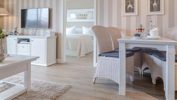 A modern living room with a flat-screen TV, white furniture, and striped wallpaper. - Viktoria Residenz 9 - Top city location: Very comfortable, light-flooded 2 (Sylt)