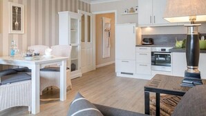A modern kitchen with white cabinets, a microwave, and a stove. There is a dining area with a white table and chairs, and a sofa in the foreground. - Viktoria Residenz 9 - Top city location: Very comfortable, light-flooded 2 (Sylt)