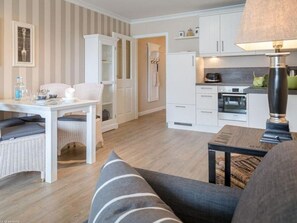 A modern kitchen with white cabinets, a microwave, and a stove. There is a dining area with a white table and chairs, and a sofa in the foreground.
