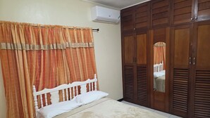 Ein Schlafzimmer mit Bett, Vorhängen, einer Klimaanlage und Holzschränken.