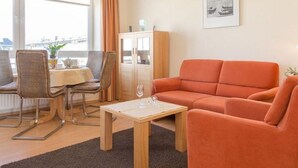 A living room with a sofa, dining table, chairs, and a cabinet. - Kurt`s Island - In Friedrichstraße: 2.5 room apartment with balcony (Sylt)