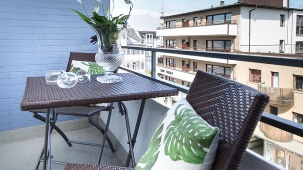 A balcony with wicker furniture, a potted plant, and a clear view of surrounding buildings. - Kurt`s Island - In Friedrichstraße: 2.5 room apartment with balcony (Sylt)
