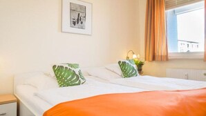 A hotel room with two beds, a nightstand, a window with curtains, and a framed picture on the wall. - Kurt`s Island - In Friedrichstraße: 2.5 room apartment with balcony (Sylt)
