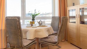 A dining area with wicker chairs, a round table, and a cabinet with glass doors. - Kurt`s Island - In Friedrichstraße: 2.5 room apartment with balcony (Sylt)