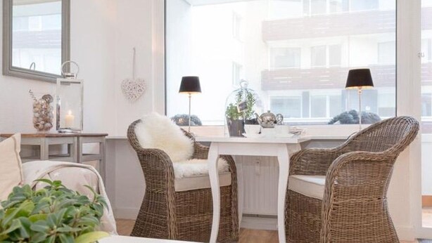 Ein modernes Wohnzimmer mit Korbstühlen, einem weißen Tisch und einem großen Fenster mit Blick auf Gebäude.