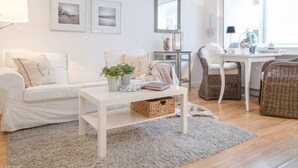 Ein modernes Wohnzimmer mit einem weißen Sofa, einem Couchtisch, Korbstühlen und einem großen Fenster, das für natürliches Licht sorgt.