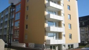 Ein mehrgeschossiges Wohngebäude mit Balkonen, einer flachen Dachterrasse und blauem Himmel.