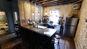 A rustic kitchen with a large island, wooden beams, and a stone wall. - Primitive yet classy apartment in rural Iowa near small town shopping and hiking (Colesburg)