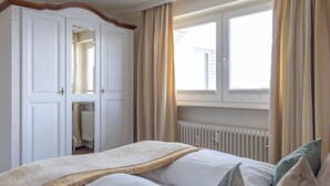A hotel room with a bed, a window with curtains, a radiator, and a wardrobe.