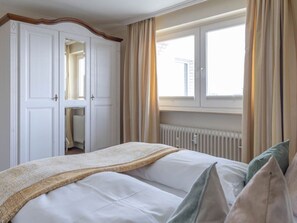 A hotel room with a bed, a window with curtains, a radiator, and a wardrobe. - Dwarslöper 2 - 2 room apartment on the beach - Outstanding sea view from the 5th floor (Sylt)