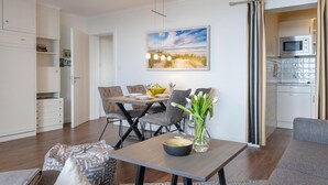 A modern living room with a dining area, a kitchen, and a view of the beach.