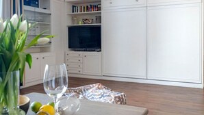 A room with a wooden floor, white cabinets, a television, and a table with a vase and glasses.
