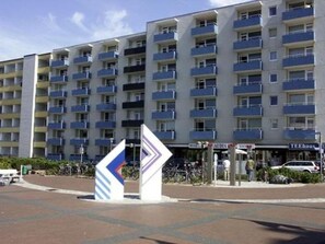 A multi-story hotel with balconies, a central plaza, and a TEEhaus store. - Dwarslöper 2 - 2 room apartment on the beach - Outstanding sea view from the 5th floor (Sylt)