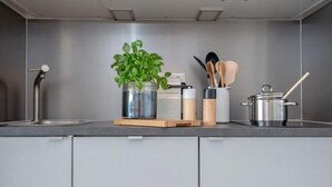 Una cocina moderna con armarios grises, una campana extractora de acero inoxidable, una planta en maceta, una tabla de cortar de madera, un especiero y una olla con una cuchara de madera.
