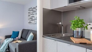 Una cocina moderna con un lavaplatos integrado, una encimera con una planta y un sofá gris en la sala.